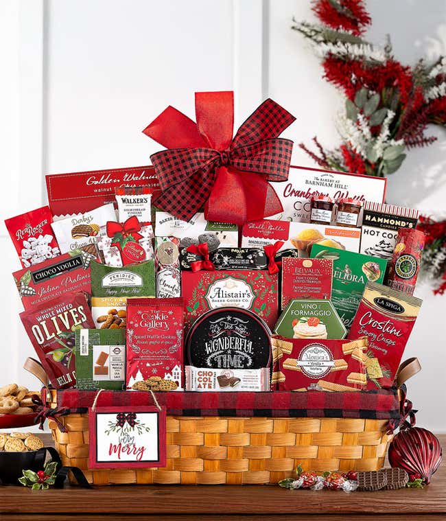  Large gift basket filled with an assortment of gourmet snacks and treats, including chocolates, cookies, crackers, lemon cakes, and more, decorated with a red and black plaid bow and a Peace &amp; Joy ornament.