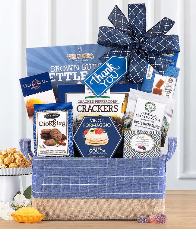 This elegant Thank You gift basket features a white tote with leather handles and a blue bow. It's filled with Tom Clark's Kettle Corn, Lindt Lindor Truffles, Vino e Formaggio Cheese Spread, Bella Campagna Olives, Ciokini cookies, and crackers. &amp;#8203;