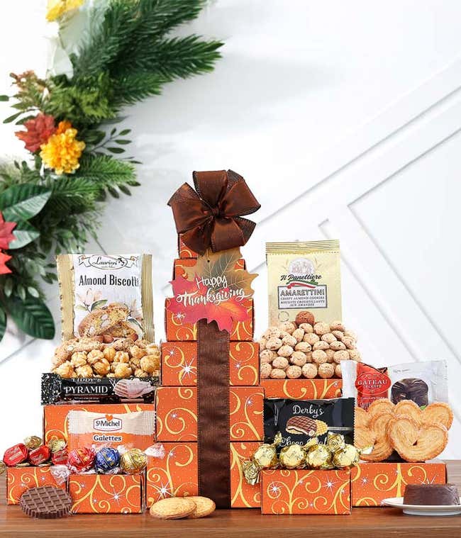 Thanksgiving gift tower with festive orange boxes filled with chocolates, cookies, and snacks, topped with a gold bow and a 
