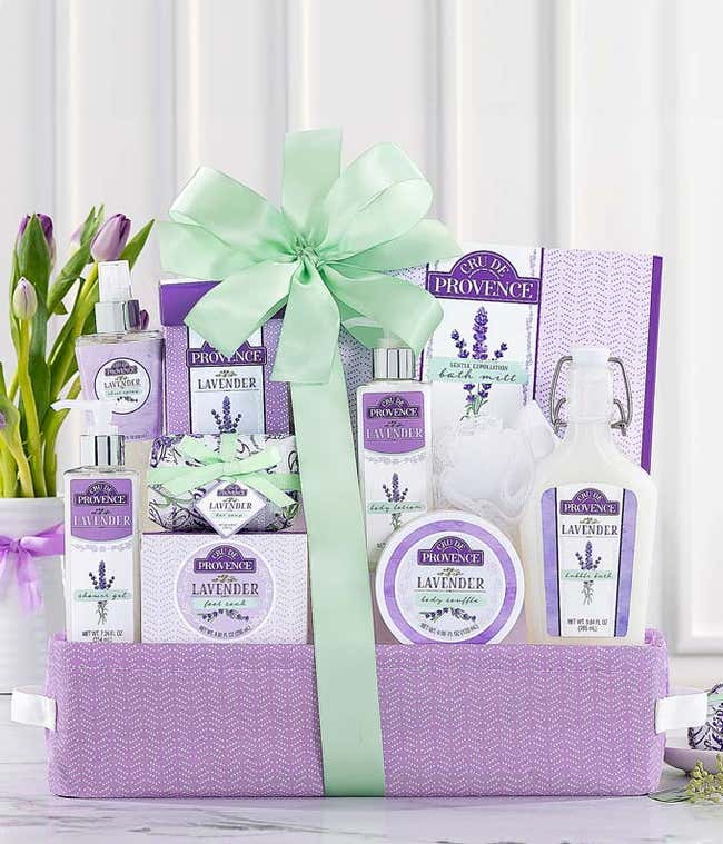 Spa gift basket featuring lavender scented sheet spray, chunky bath salts, bubble bath, body butter, shower gel, and more in a lavender colored gift basket with a green ribbon