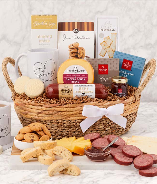 Sympathy gift basket in a woven tray with sausage, cheeses, flatbread, cookies, almond anise biscotti, tea, honey, two white mugs with Cup of Comfort design, and a white ribbon, displayed with a serving of meats, cheeses, cookies, and tea.