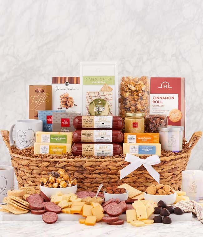 Sympathy gift basket with gourmet cheeses, beef summer sausages, crackers, popcorn, cookies, truffles, candles, and two white mugs in a woven basket with a sympathy ribbon.
