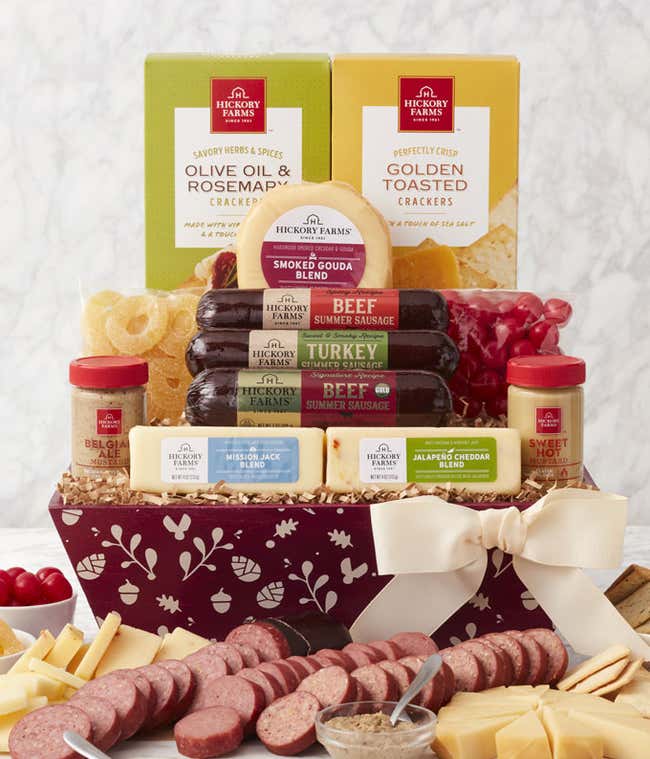 Fall holiday gift box with sausages, cheeses, crackers, mustards, and dried pineapple, tied with a cream bow and displayed with sliced meats and cheeses.