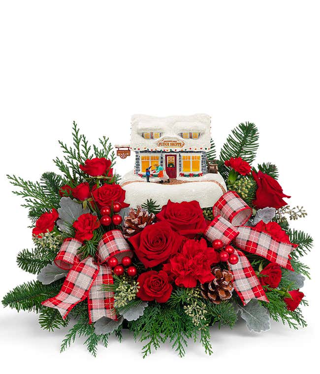 Centerpiece of red roses and carnations, filled out with Christmas greenery, and accented with red berry picks, pinecones, and ribbons, with a Thomas Kinkade Fudge Shoppe collectible in the middle