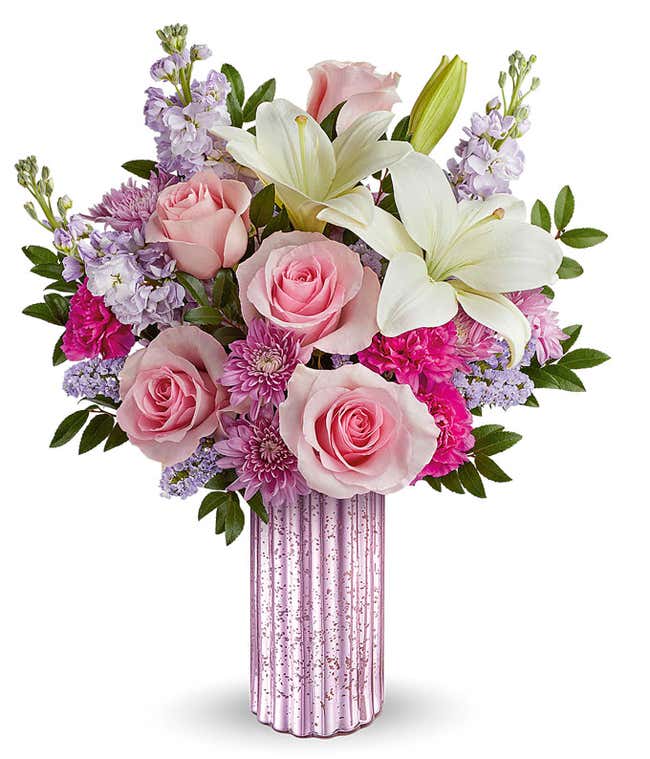 Image of a Mother's Day arrangement featuring Pink Roses, White Asiatic Lilies, Hot Pink Carnations, Lavender Stock, Lavender Cushion Spray Chrysanthemums, floral greenery, all beautifully presented in a metallic lavender vase.