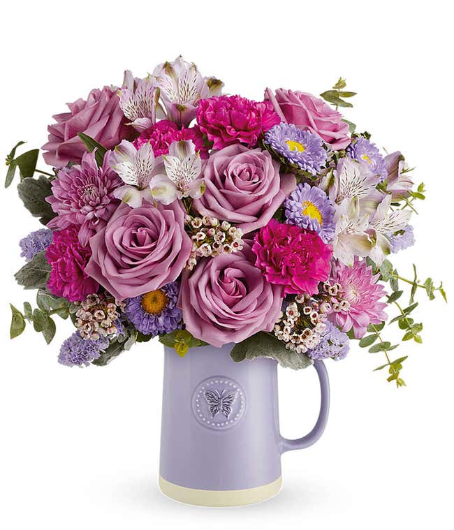 Image of a Mother's Day arrangement featuring Lavender Roses, Lavender Alstroemeria, Fuchsia Carnations, Lavender Matsumoto Asters, Lavender Cushion Spray Chrysanthemums, Lavender Sinuata Statice, Pink Waxflower, floral greens, all beautifully presented i
