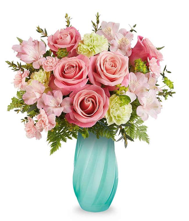 Coral roses, pink alstroemeria, green carnations, mini pink carnations, and floral greenery in a tall aqua swirled vase