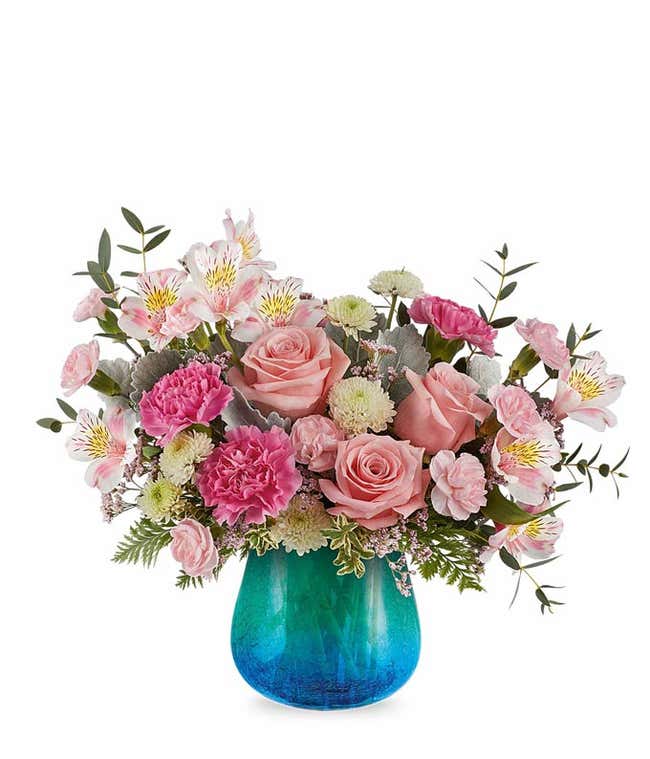 Pink roses, pink alstroemeria, pink carnations, white cushion poms, and floral greenery in a blue &amp; green ombre glass vase