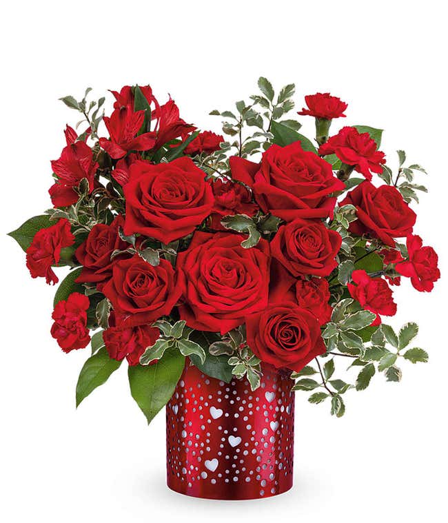 Valentine&rsquo;s Day arrangement of classic red roses with lush greenery displayed in a red cylinder vase heart cutouts