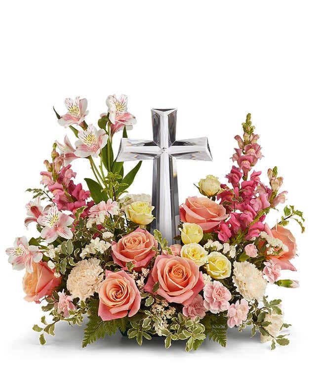 Coral roses, yellow spray roses, pink alstroemeria, creme carnations, mini pink carnations, hot pink snapdragons, and floral greenery with a large crystal cross on top of the arrangement