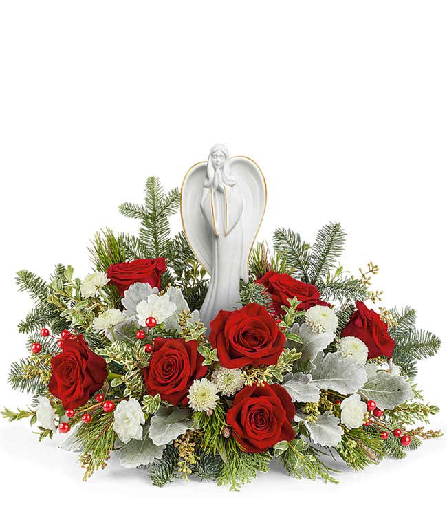 Floral centerpiece featuring red roses, white flowers, silver-hued foliage, and evergreen sprigs, with a serene angel figurine standing in the center.