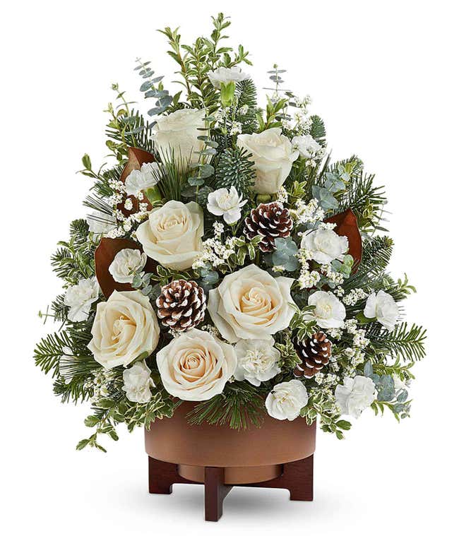 Christmas tree-shaped floral arrangement with white roses, white carnations, white limonium, frosted pinecones, seasonal greenery, and eucalyptus in a brown ceramic container.