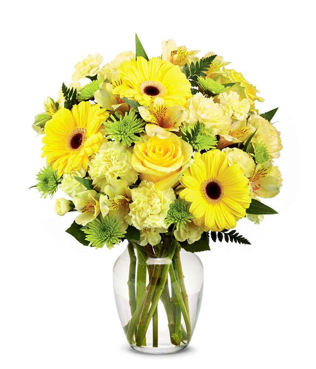 A floral arrangement featuring yellow gerbera daisies, yellow carnations, yellow mini carnations, yellow roses (deluxe &amp; premium), and yellow alstroemeria in a glass vase.