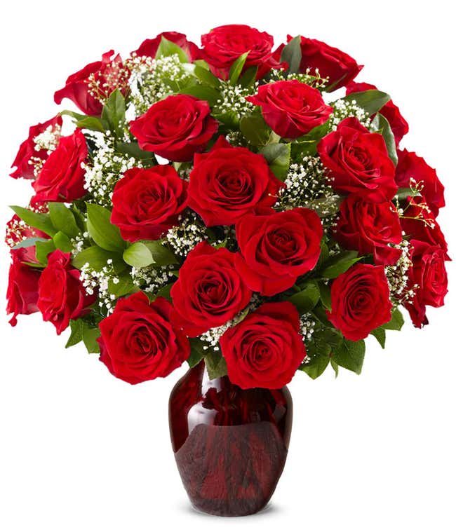 Red rose bouquet with baby's breath and greenery arranged in a deep red glass vase.