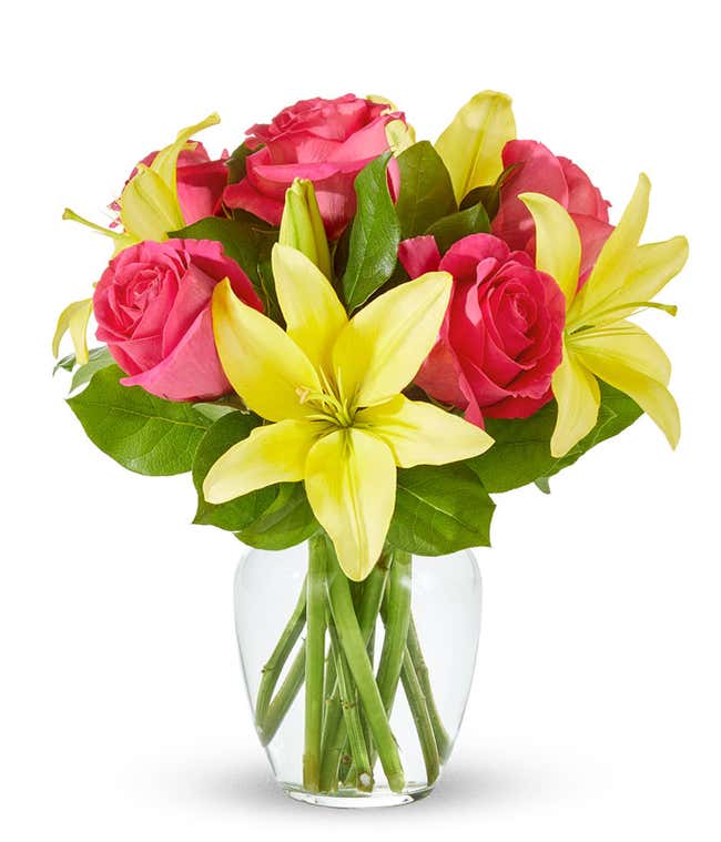 An arrangement featuring yellow lilies and pink roses in a clear glass vase.
