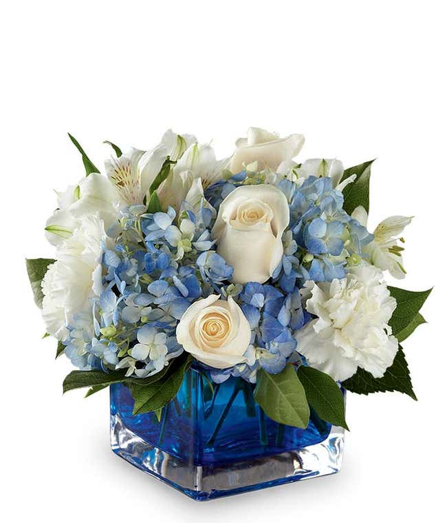 A serene arrangement featuring white carnations, white roses, white alstroemeria, and blue hydrangea, elegantly presented in a blue cube vase.
