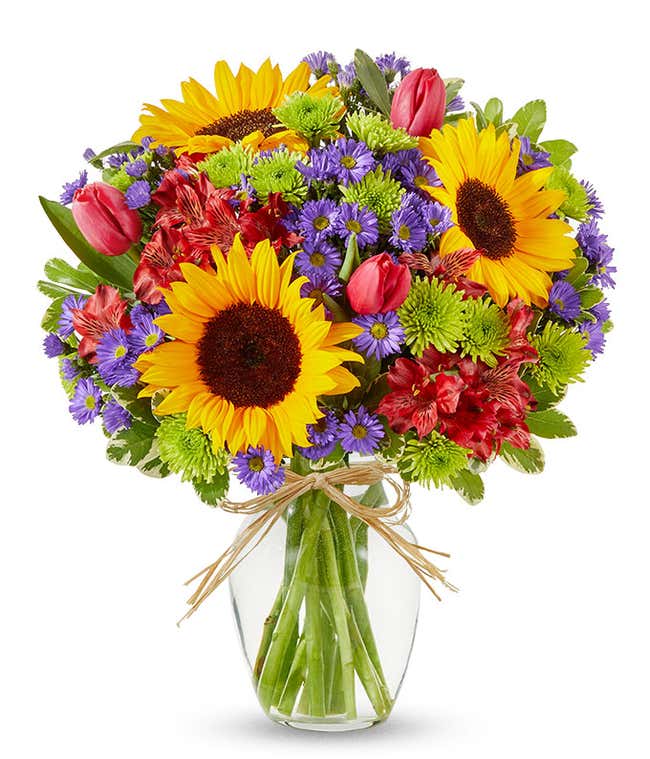 Sunflowers and pastel flowers in a clear glass vase with raffia tie