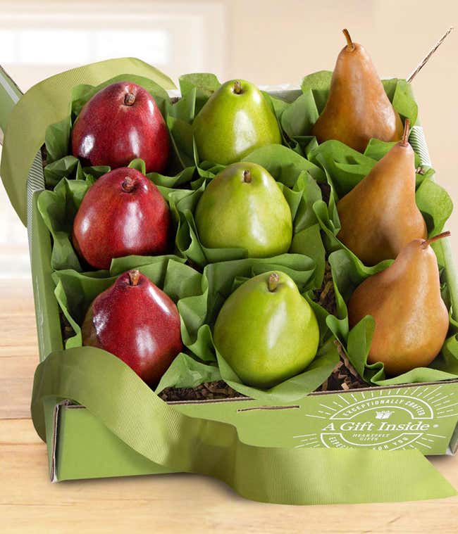 A green box containing three varieties of pears: red, green, and brown, each nestled in green tissue paper, decorated with a green ribbon. 