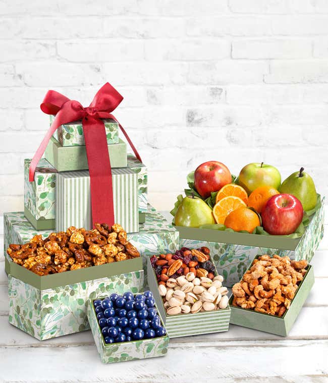 A gift tower with multiple green boxes containing fresh fruits, nuts, and chocolates, tied with a red ribbon.