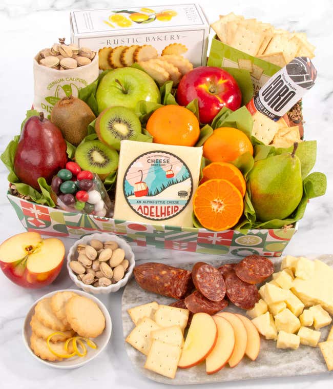 A gourmet holiday basket featuring fresh apples, pears, and oranges alongside artisan cheese, crackers, salami, pistachios, and festive candies.