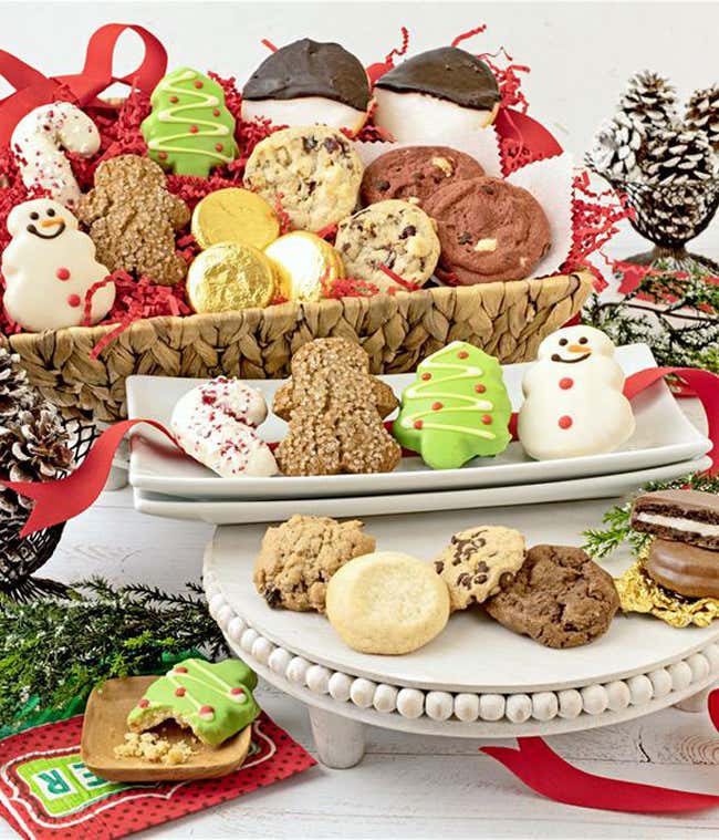  Assorted Christmas-themed cookies including gingerbread men, snowmen, Christmas trees, chocolate-dipped cookies, and gold chocolate coins arranged in a festive basket and on plates, with decorative pinecones and red ribbons in the background