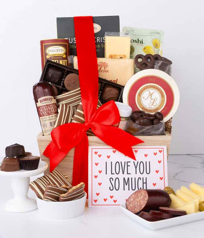 A wooden basket filled with chocolates, summer sausage, cheeses, crackers, crisps, mustard, and snacks, with displays of chocolate treats, sliced sausage, olives, and cheese arranged with a Season's Greetings message.