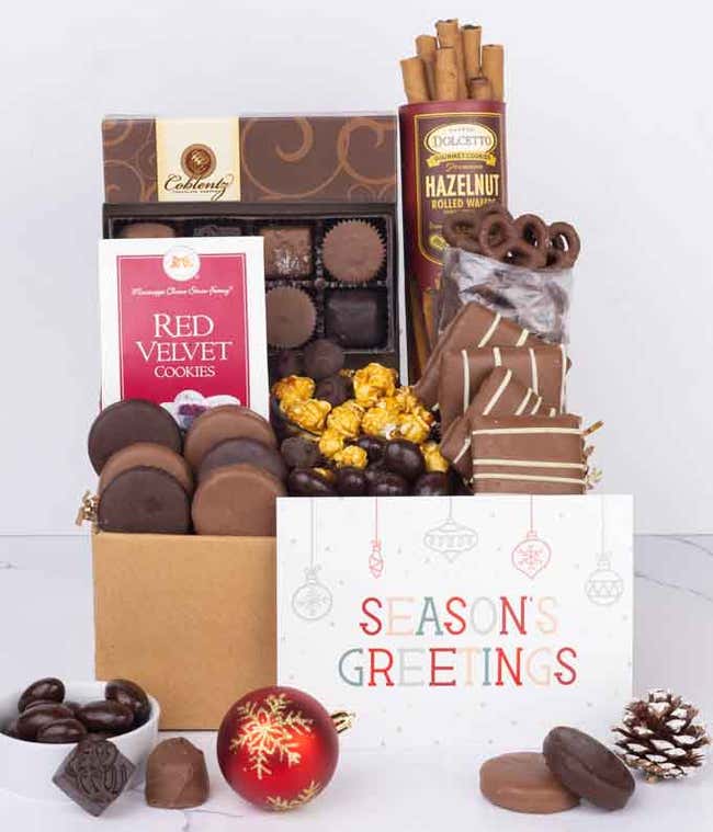 A gift box overflowing with treats including an assortment of chocolate-covered items like oreoes, almonds, graham crackers and pretzels along with red velvet cookies, hazelnut wafers, an 8-piece box of chocolates and a Season's Greetings card.