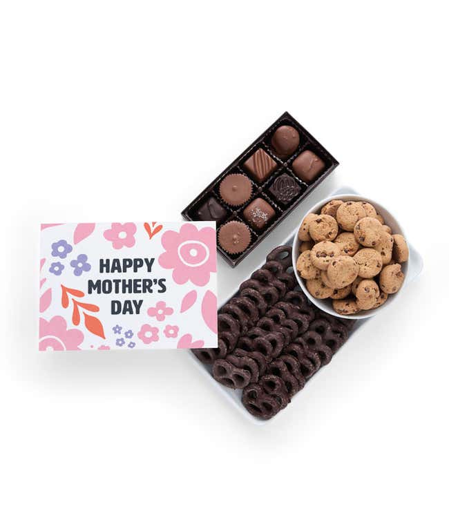 A gift filled with chocolate-covered pretzels, mini chocolate chip cookies, and a box of assorted chocolates. A card reading 'Happy Mother's Day' rests beside the treats.