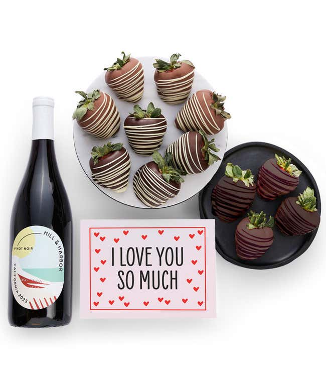 A bottle of Hill &amp; Harbor California Pinot Noir is displayed beside 12 assorted chocolate-covered strawberries, drizzled in milk and dark chocolate and a card saying, 'I Love You'.