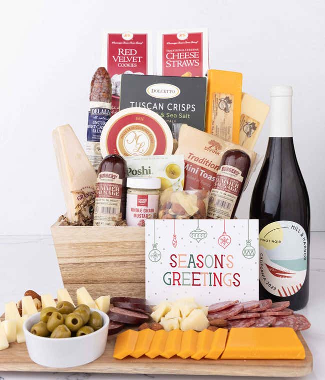 Wooden basket filled with 4 cheeses, 3 sausages, crackers, cookies, nuts, mustard, olives and crisps alongside a bottle of Hill &amp; Harbor Pinot Noir and Season's Greetings message.