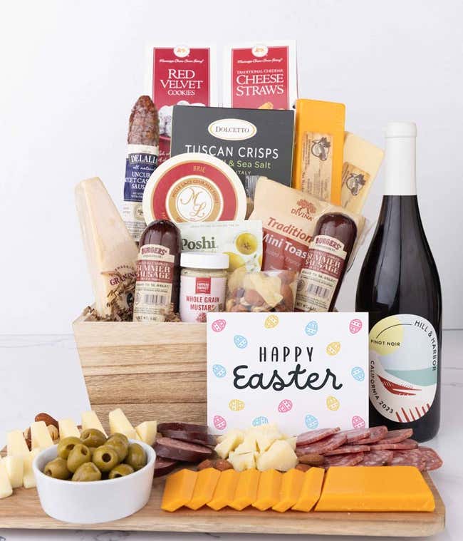 A wooden gift basket filled with summer sausages, 3 cheeses, Tuscan crisps, mini toasts, red velvet cookies, cheese straws, nuts, mustard, and a bottle of wine with an Easter card.
