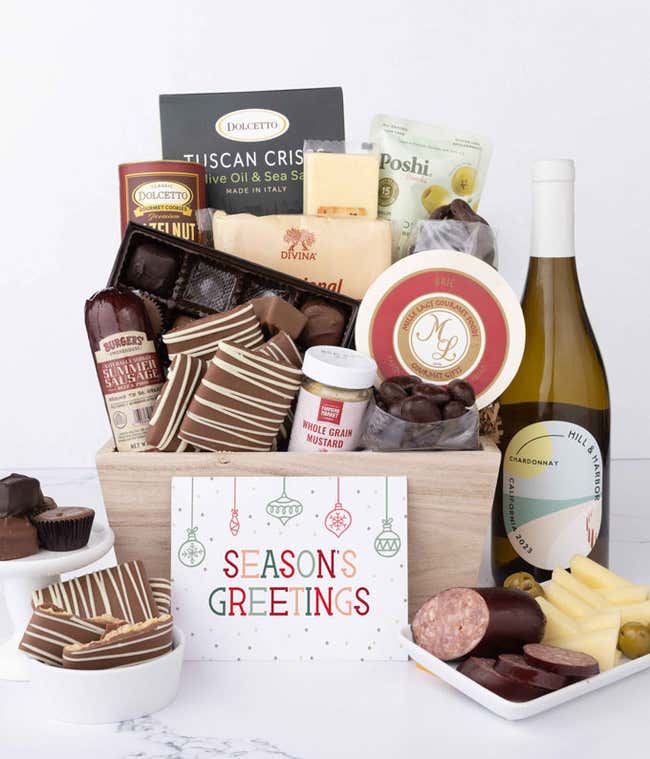 A wooden basket filled with chocolates, summer sausage, cheeses, crackers, crisps, mustard, and snacks, with displays of chocolate treats, sliced sausage, olives, and cheese arranged with a bottle of wine and Season's Greetings message.