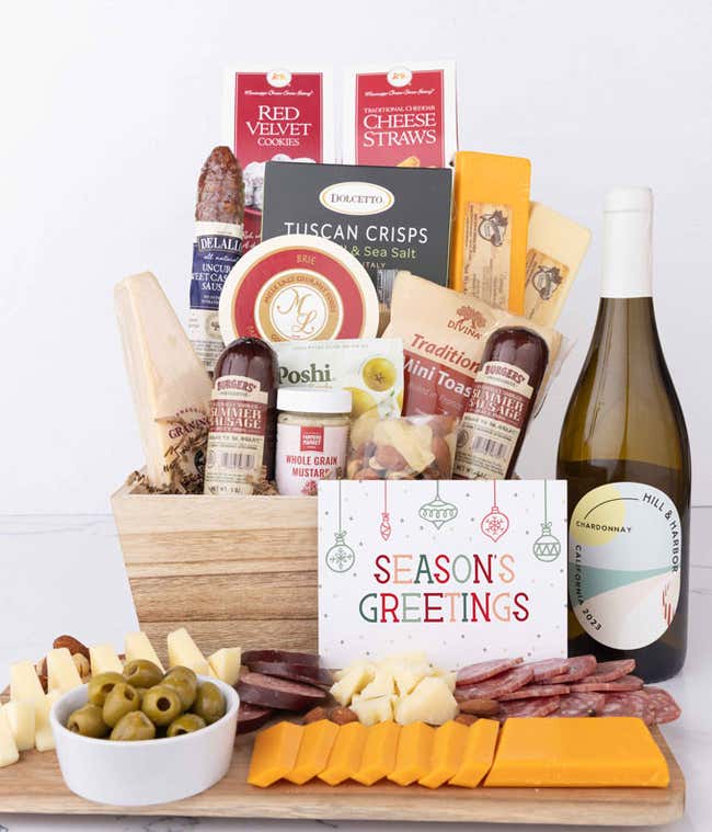 Wooden basket filled with 4 cheeses, 3 sausages, crackers, cookies, nuts, mustard, olives and crisps alongside a bottle of Hill &amp; Harbor Chardonnay and Season's Greetings message.