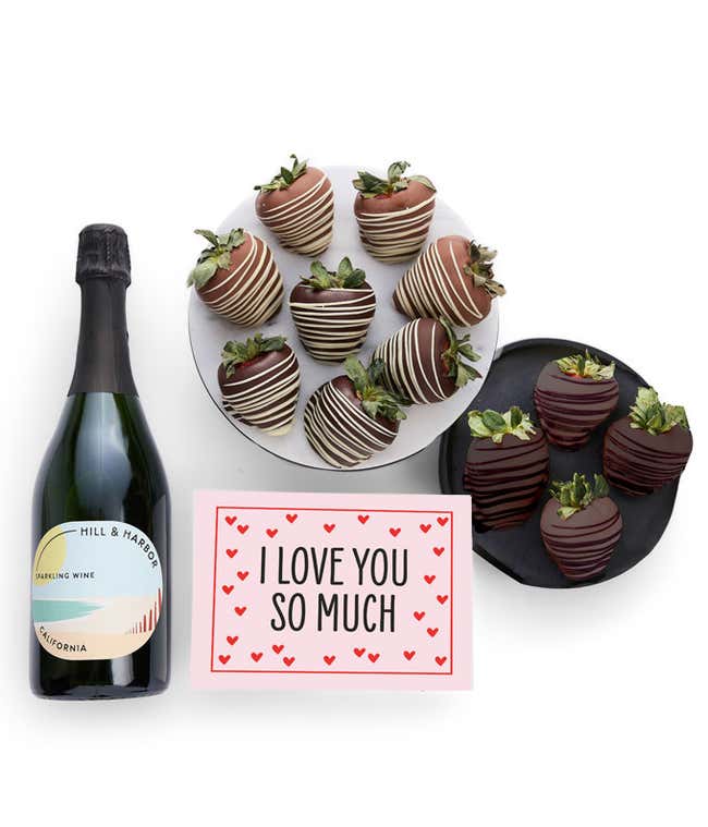 A bottle of Hill &amp; Harbor California Sparkling Wine is displayed beside 12 assorted chocolate-covered strawberries, drizzled in milk and dark chocolate and a card saying, 'I Love You'.