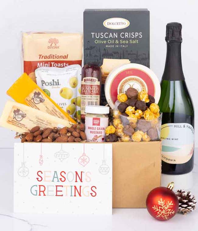 A charcuterie gift set with 3 cheeses, Tuscan crisps, focaccia crackers, olives, mustard, smoked almonds, chocolate-covered popcorn, summer sausage, a bottle of California Sparkling wine, and a Season&rsquo;s Greetings card.