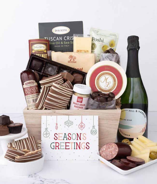 A wooden basket filled with chocolates, summer sausage, cheeses, crackers, crisps, mustard, and snacks, with displays of chocolate treats, sliced sausage, olives, and cheese arranged with a bottle of wine and Season's Greetings message.