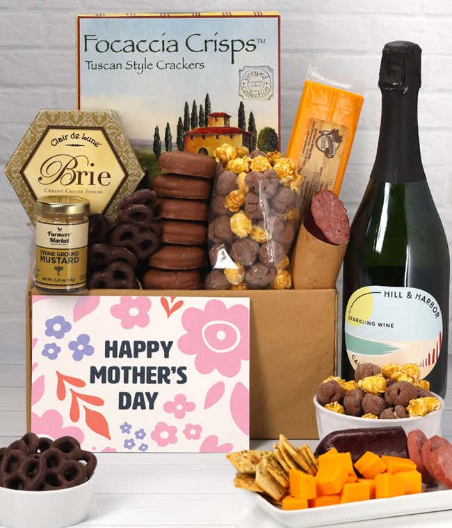 A spread featuring Hill &amp; Harbor sparkling wine, 2 cheeses, summer sausage, crackers, chocolate pretzels, caramel corn, and chocolate covered Oreos with a 'Happy Mother's Day' card.