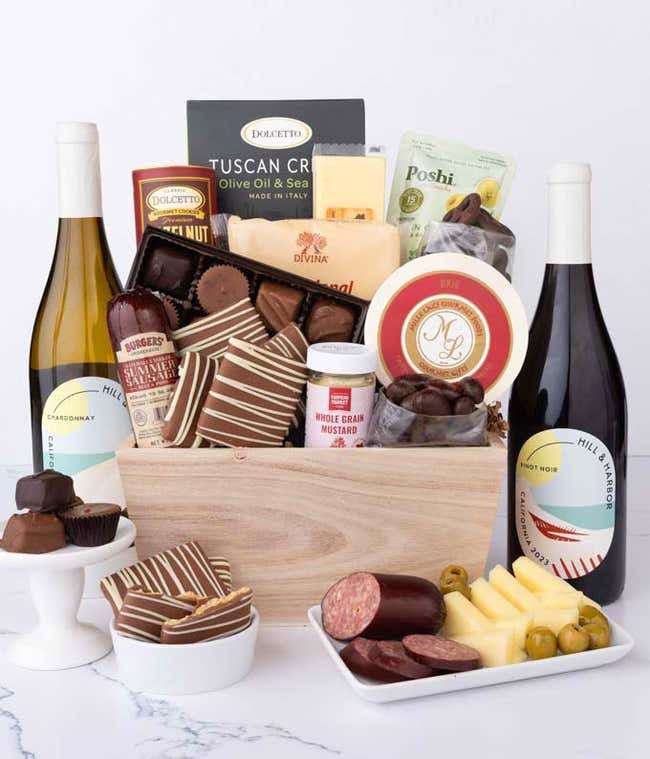 Wooden crate filled with gourmet snacks and two bottles of Hill &amp; Harbor wine,  Chardonnay and Pinot Noir, alongside artisan summer sausage, creamy cheeses, assorted chocolates, striped chocolate-covered grahams, cookies, crisps, mustard, and olives.