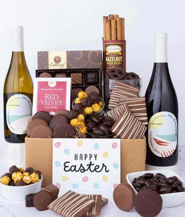 Two bottles of wine are surrounded by an assortment of chocolate treats, including chocolate-covered pretzels, assorted chocolates, chocolate chip cookies, mini buckeyes, caramel popcorn, chocolate-covered Oreos and finished with a Happy Easter card.