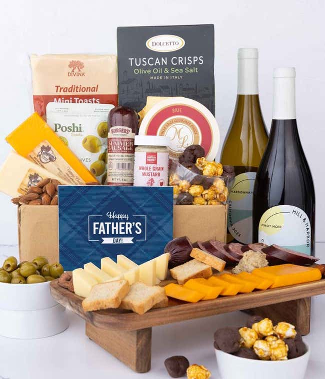 Two bottles of wine with gourmet charcuterie including Tuscan crisps, focaccia crackers, brie, mustard, sausage, 3 cheeses, olives, smoked almonds, and chocolate-covered treats, complete with a 'Happy Father's Day' card.