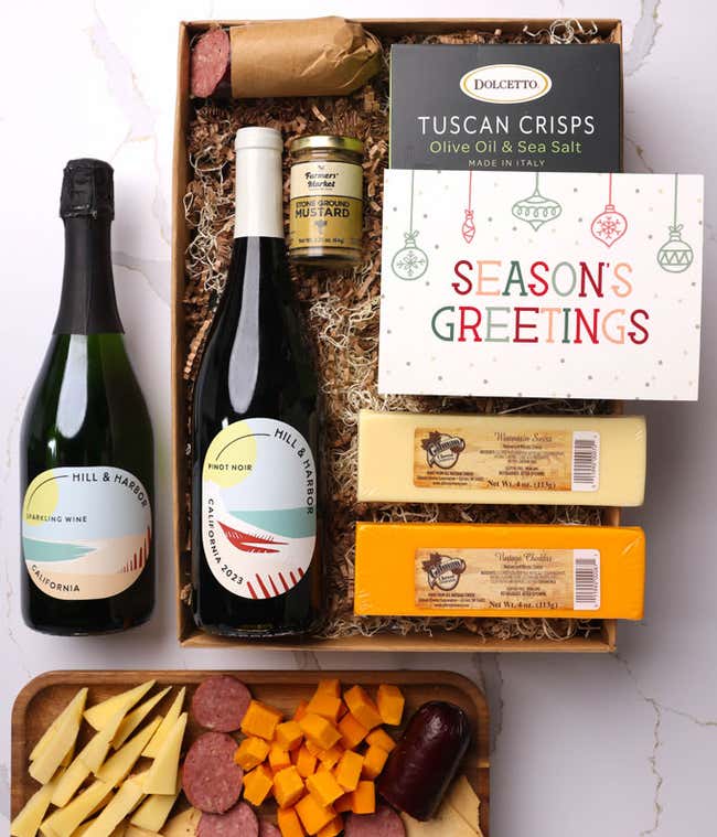 A gift box with two bottles of California wine (Pinot Noir and Sparkling Wine), two types of cheese, crackers, stone-ground mustard, a summer sausage, and a 'Season's Greetings' card.