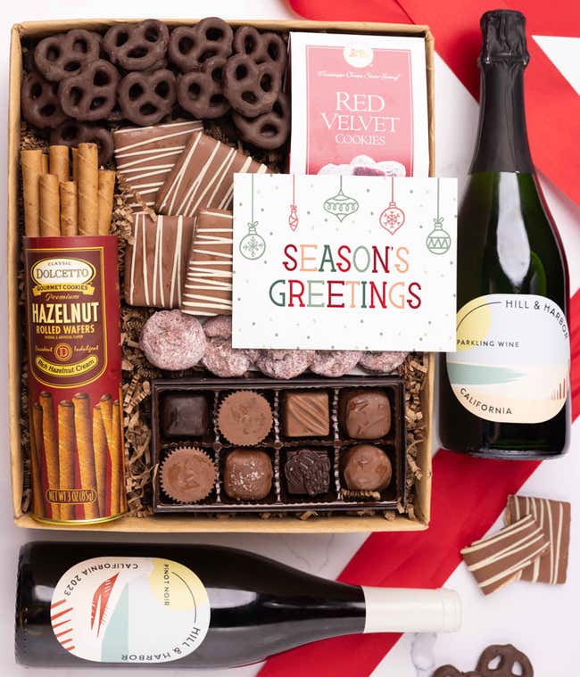 A holiday gift set with two bottles of Hill &amp; Harbor wine (Pinot Noir and Sparkling Wine), a box of assorted chocolates, a tray of chocolate-covered pretzels, a bowl of mini chocolate chip cookies, and a Season's Greetings message card.