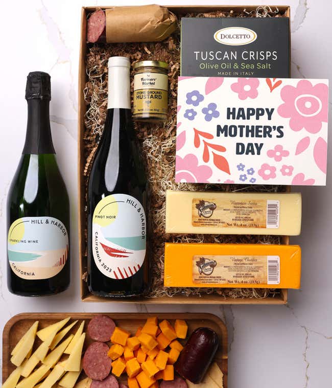 A snack and wine gift box featuring 2 bottles of wine - red and sparkling, 2 cheeses - chaddar &amp; Swiss, cracker crisps, summer sausage, and mustard. A 'Happy Mother's Day,' sits on top. A perfect gift for Mom.