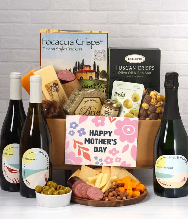 A charcuterie spread with 3 cheeses, sausage, olives, crackers, mustard, almonds, and chocolate finished with bottles of red, white &amp; sparkling wine and 'Happy Mother's Day' card.