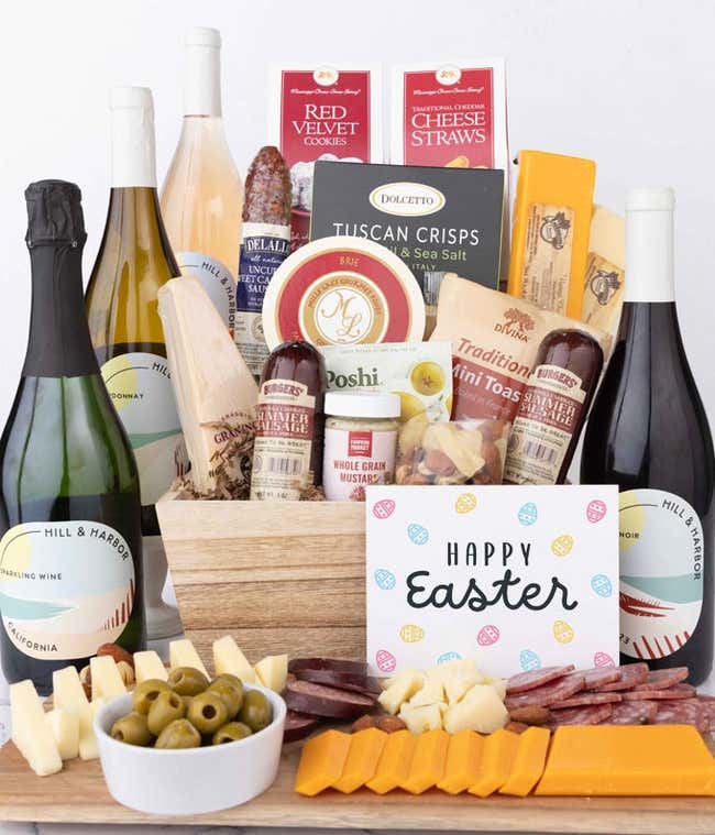 A wooden gift basket filled with summer sausages, 3 cheeses, Tuscan crisps, mini toasts, red velvet cookies, cheese straws, nuts, mustard, and 4 bottles of wine with an Easter card.